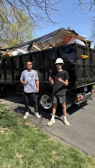 Crew standing beside a dump truck loaded to the top with construction debris and cardboard